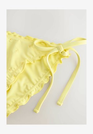 Gul bikiniunderdel med volanger, snörning och texturerad yta med små broderade detaljer. Mjuk, stretchy tyg.
