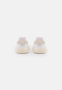 Låga sneakers med ett övre av vitt läder, beige mockadetaljer vid hälen och en texturerad gummisula med ingraverat varumärkesnamn.