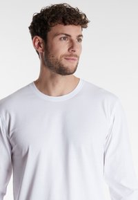 Long-sleeve white T-shirt in lightweight cotton, featuring a round neck and simple design. Smooth texture, minimal stitching details.