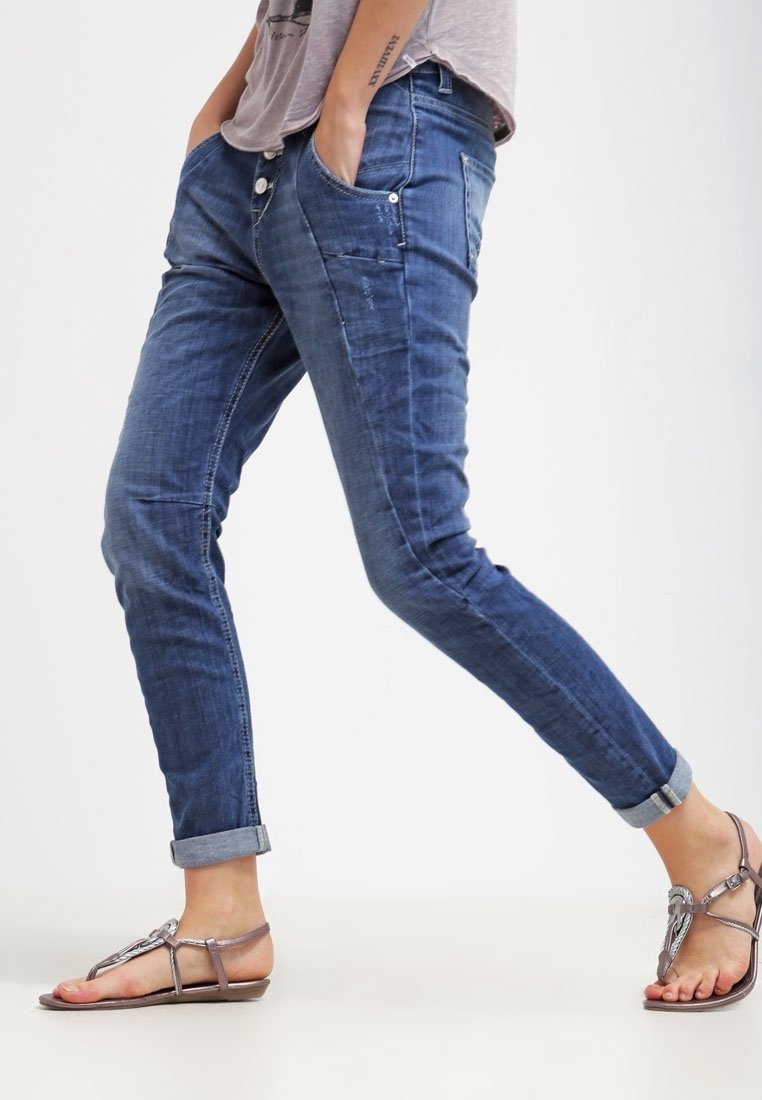 Slim-fit dżinsy w ciemnoniebieskim denimu z delikatnym przecieraniem, pięć kieszeni i podwinięte mankiety, w zestawieniu z metalowymi sandałami.