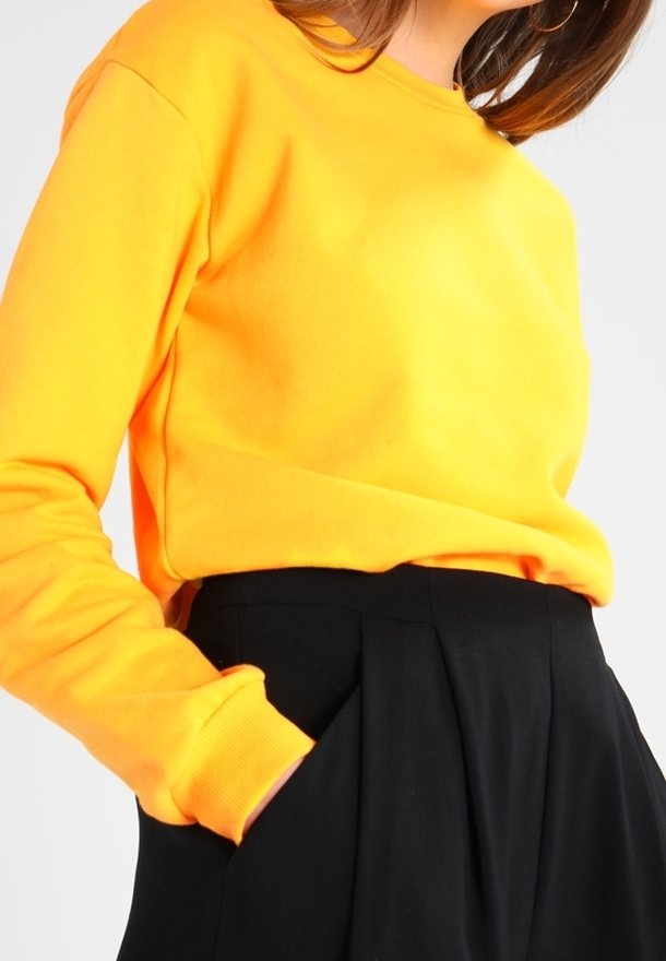 Sudadera amarilla brillante con cuello redondo y mangas largas, usada sobre pantalones negros de cintura alta, con un ajuste relajado.