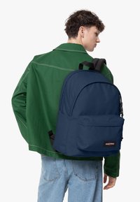 Mochila Eastpak de color azul marino con un gran compartimento principal y un bolsillo frontal, con correas negras y un parche de marca. Textura de tejido suave.
