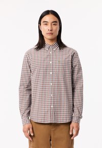 Camisa de cuadros marrón y blanca con cuello, mangas largas, un bolsillo en el pecho y un pequeño detalle de logo verde en el lado izquierdo del pecho.