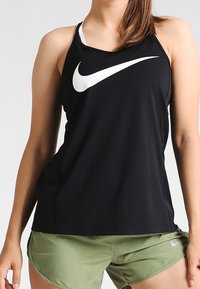 Sort atletisk tanktop med hvidt Nike-logo, med racerback-design. Kombineret med lysegrønne shorts med et subtilt mønster.