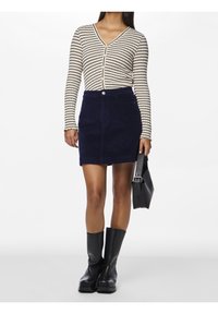 Randig långärmad knäppskjorta i krämfärg och marinblå, matchad med en mörk marinblå kordflorskort. Svarta knähöga stövlar och en svart väska fulländar looken.