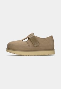 Beige suède schoen met een ronde neus, verstelbare band en duurzame rubberen zool. Beschikt over een uitsnijding ontwerp op de bovenkant voor ventilatie.