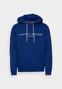 Sudadera azul con capucha, con un bolsillo frontal, cordones blancos y "TOMMY HILFIGER EST. 1985" impreso en blanco en el pecho.