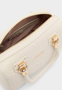 Borsa a tracolla beige in tessuto con cerniera superiore, hardware dorato e logo impresso. L'interno rivela foderato in tessuto chiaro e una piccola tasca.