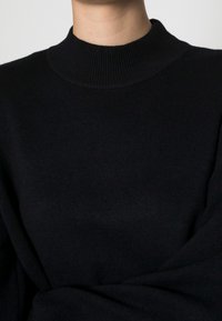 Schwarzer Strickpullover mit einem gerippten Rollkragen und langen Ärmeln, der aus einem weichen, strukturierten Stoff besteht und eine lässige Passform bietet.