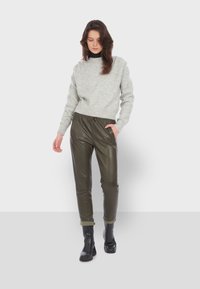 Světle šedý pletený svetr s vysokým límcem, doplněný olivově zelenými joggers z umělé kůže se všitou gumou v pase a bočními kapsami. Černé kotníkové boty.