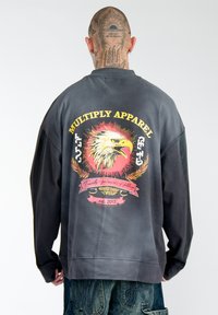 Schwarzer Sweatshirt mit einem Verlaufs-Effekt, versehen mit einem farbenfrohen Adler-Graphic und dem Text "MULTIPLY APPAREL" auf der Rückseite. Bequeme Passform.