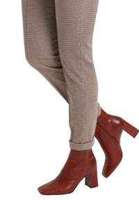 Pantalon marron à carreaux, coupe slim, associé à des bottines en cuir marron foncé avec un talon bloc et un bout carré.