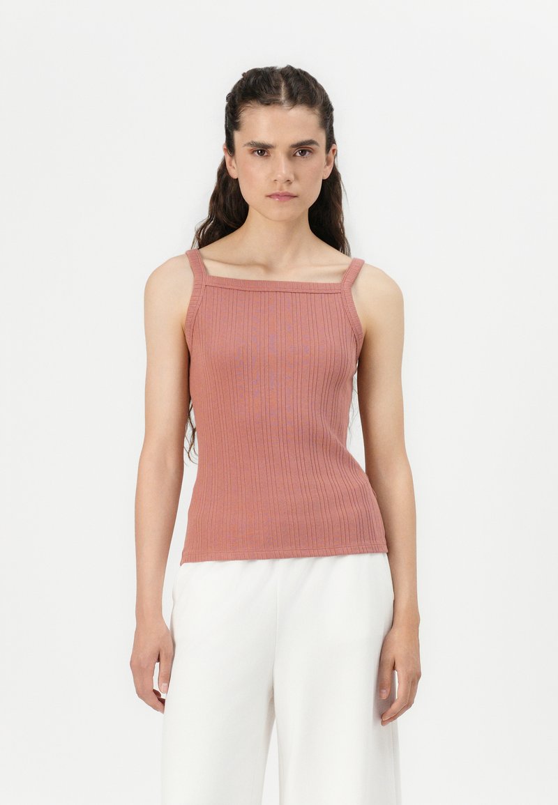 Ribbed, fitted tank top in dusty rose, featuring wide straps and a squared neckline. Pairing with flowy white pants enhances simplicity.