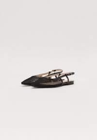 Ballet flats noires en maille avec un bout pointu, présentant un design texturé et une fine lanière de cheville pour un maintien sécurisé. Semelle intérieure brune minimaliste.