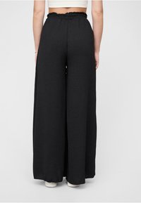 Black wide-leg pants with a ruffled waistband, made of soft fabric. The design features a loose fit and elastic around the waist.