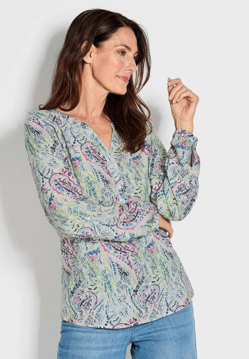 Langärmlige Bluse aus leicht grünem Stoff mit einem Paisleymuster in rosa und blauen Tönen, mit einem V-Ausschnitt und Knopfdetails.