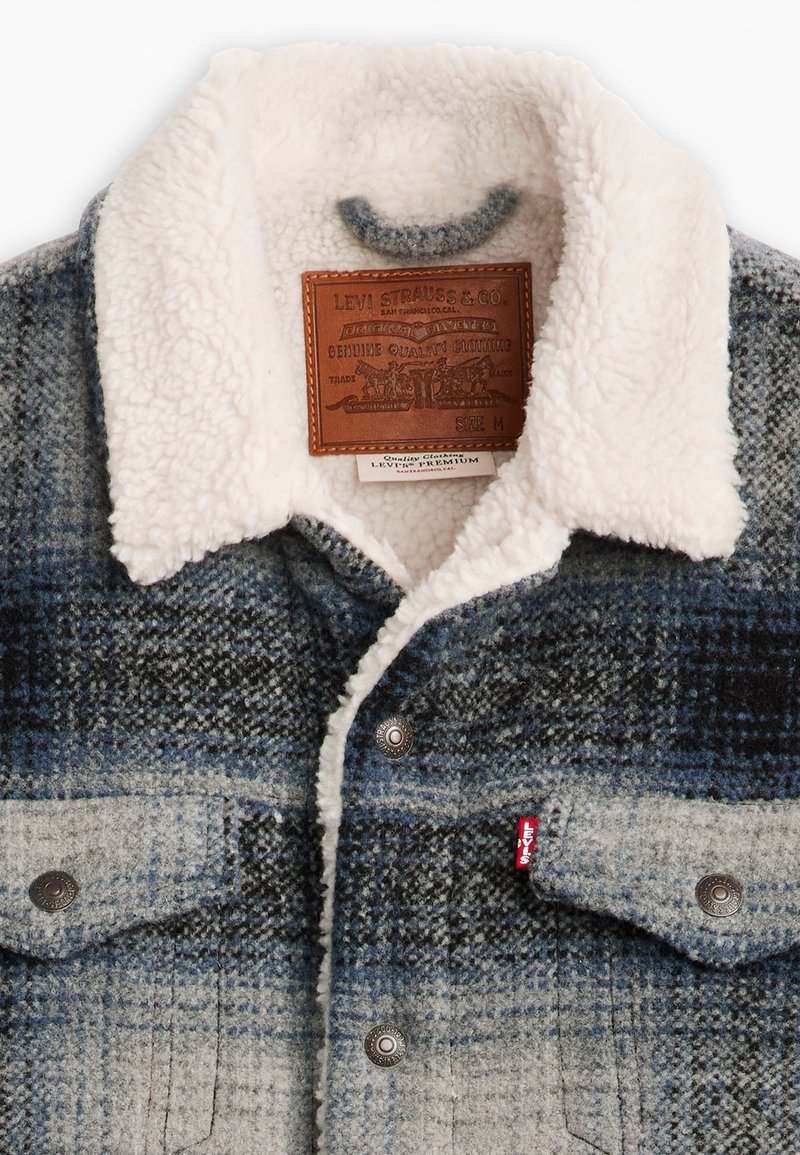 Veste en jean à carreaux dans des tons de bleu et de gris, dotée d'un col en fausse fourrure et de poches avant avec des pressions en métal. Étiquette du logo Levi's visible.