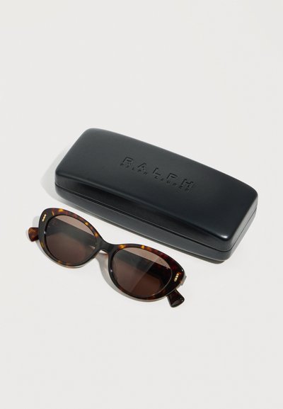 Οβάλ γυαλιά ηλίου με φλοιδωτό μοτίβο και σκούρους φακούς δίπλα σε μια μαύρη σκληρή θήκη με λογότυπο Ralph Lauren σε λευκό φόντο.