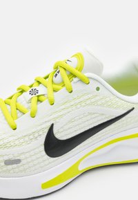 Běžecká obuv Nike s vrchní částí ze bílé a neonově žluté pleteniny, černým logem Swoosh a žlutými akcenty na podešvi a tkaničkách.