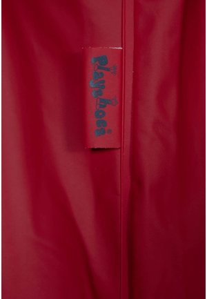 Imperméable rouge avec une texture lisse. Dispose d'une étiquette bleue portant la mention "Playshoes", attachée à la couture. Design simple et fonctionnel.