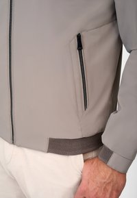 Light gray jacket with a smooth, matte finish, featuring a side zippered pocket and mesh-textured cuffs and hem.