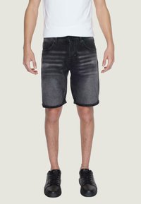 Shorts in denim nero con una finitura sbiadita, orli arrotolati e design a cinque tasche, abbinati a sneakers nere e una maglietta bianca.