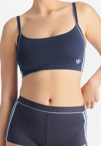 Marinblå sportbehå med ljusblå detaljer, tillverkad av mjukt tyg, med tunna remmar och en logotyp på vänster sida.