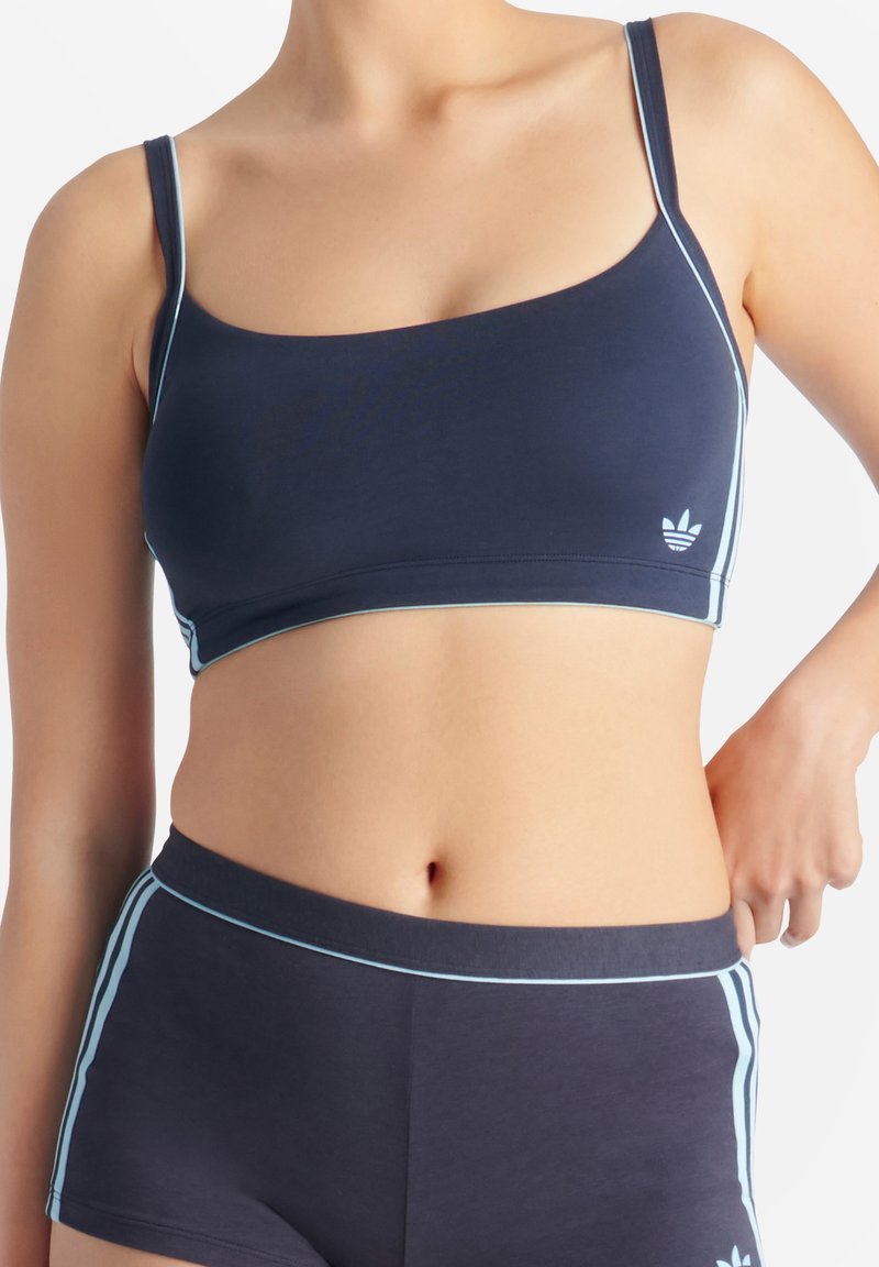 Marinblå sportbehå med ljusblå detaljer, tillverkad av mjukt tyg, med tunna remmar och en logotyp på vänster sida.