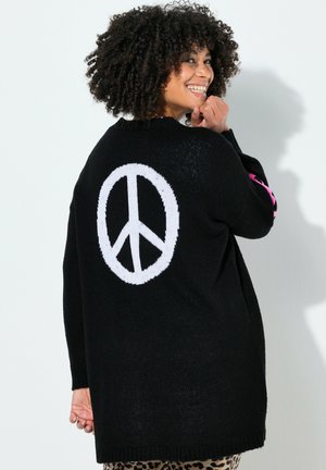Schwarzer Strickpullover mit einem großen weißen Friedenssymbol auf dem Rücken. Er hat rosa Akzente an den Ärmeln und eine lockere Passform.