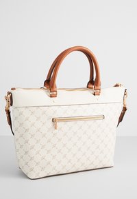 Sac cabas crème avec anses en cuir marron, poche zippée dorée à l'avant et motif répétitif subtil sur la surface texturée.