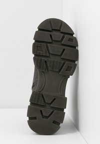 Semelle de sneaker en caoutchouc noir avec un motif texturé, dotée de crampons multidirectionnels pour l'adhérence et d'un talon rond pour la stabilité.