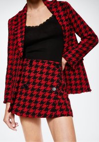 Blazer y falda a juego con patrón de pata de gallo en rojo y negro, confeccionados en tejido texturizado, con botones dobles y bordes deshilachados.