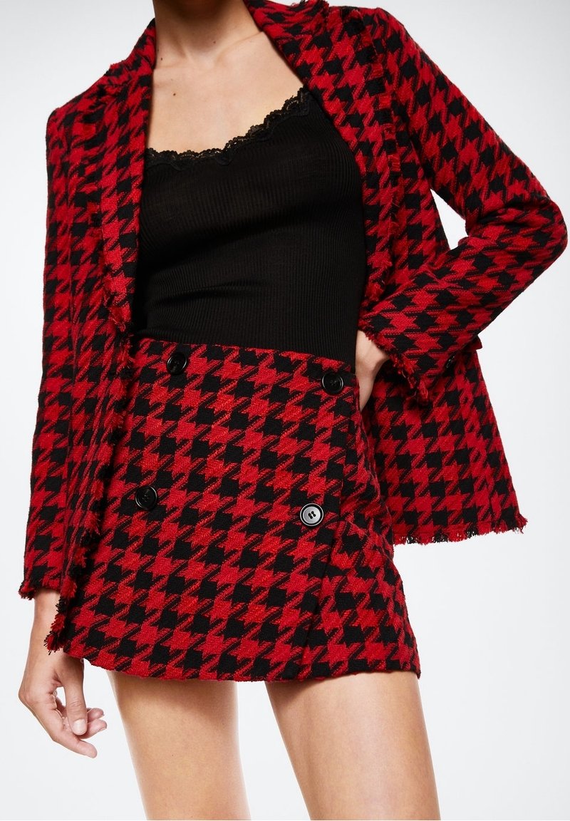 Blazer y falda a juego con patrón de pata de gallo en rojo y negro, confeccionados en tejido texturizado, con botones dobles y bordes deshilachados.