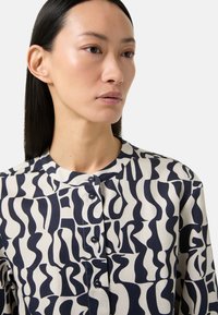 Blouse in crèmekleur met marineblauwe abstracte print, met een knoopsluiting en een ronde halslijn. Soepele stof met een lichtgewicht textuur.