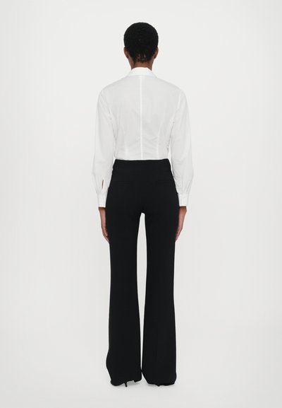 Witte fitted blouse met lange mouwen en achternaden, gecombineerd met zwarte high-waisted broek met een rechte pijp.