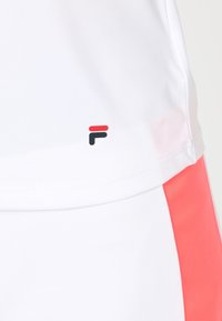 Vit idrottströja med en slät textur, med en logotyp i röd och svart accent nära fållen. Ljusröd sidpaneldetalj.