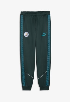Pantalon de sport vert foncé avec des bandes latérales à motifs bleus, logo de Manchester City sur la cuisse gauche, et logo Puma bleu avec "KING" sur la cuisse droite.