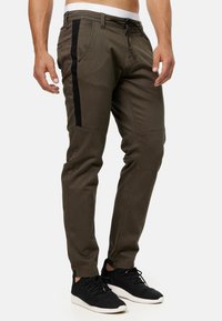 Pantalones ajustados color verde oliva hechos de una mezcla de algodón. Con paneles laterales negros, cintura con cordón ajustable y detalles con cremallera en los tobillos.