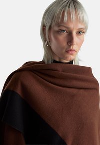 Hnědý a černý šátek z měkké látky s hladkou texturou, elegantně přehnutý. Má vrstvený design a kontrastní detaily.