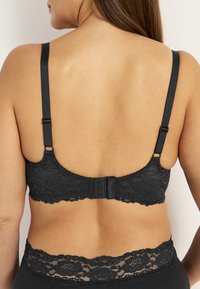 Mustan pitsin rintaliivit, joissa on säädettävät hihnat, hakasuljenta selässä ja herkät kukkakuviot pitsin yksityiskohdissa.