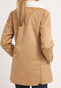 Tan faux suede takki, jossa on pehmeä valkoinen karvakaulus ja hihansuut, suoran leikkauksen ja pitkät hihat, nähtynä takaa.