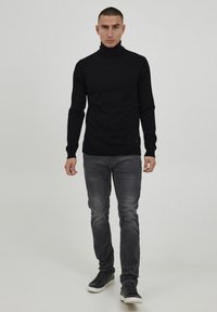 Svart høyhalset genser, slim fit, lange ermer; kombinert med grå jeans og svarte joggesko. Enkelt design, ingen synlige mønstre eller detaljer.