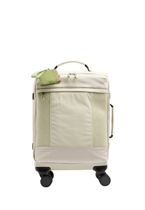 Beżowa walizka z przednimi kieszeniami z siateczki, górnymi i bocznymi uchwytami, czterema czarnymi kółkami oraz małą zieloną saszetką na suwak przymocowaną do górnej rączki.