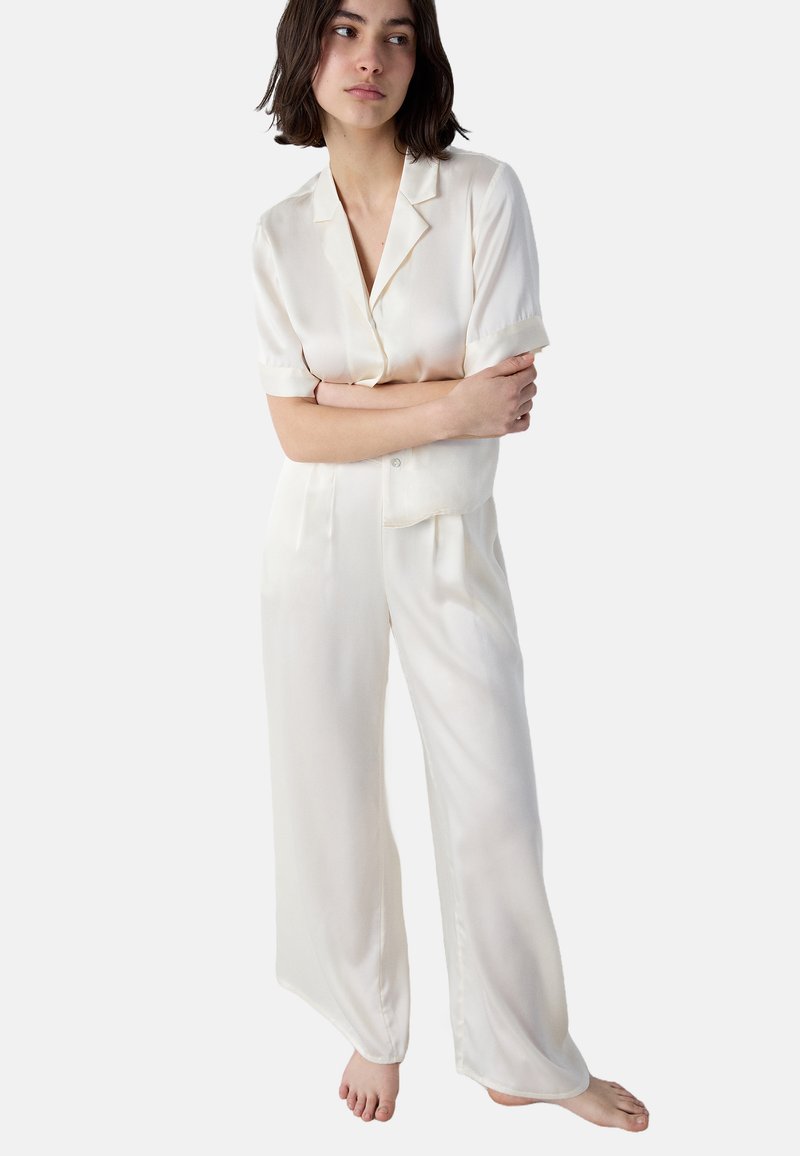 Crème-kleurige satijnen pyjama set met een kortärmige button-up top en wijdvallende broek, voorzien van een borstzak en een zachte, gladde textuur.