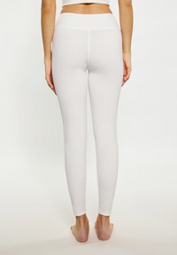 Witte, nauwsluitende leggings met een gladde textuur, hoge tailleband en ontwerp met volle lengte, weergegeven vanachter op blote voeten.