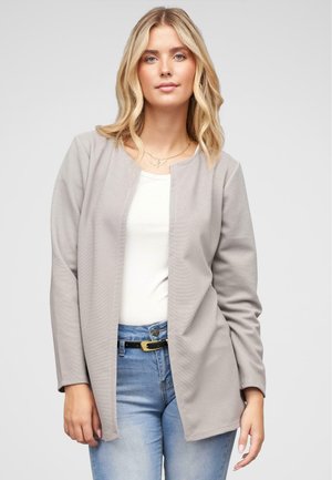 Šedý rebrovaný blazer s otvoreným predným dizajnom a dlhými rukávmi, skombinovaný s bielym topom a modrými džínsami. Obsahuje akcent čierneho opasku.