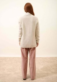 Suéter texturizado de color gris claro con cuello de chal, combinado con pantalones rectos de color rosa apagado. El fondo es neutral y suave.