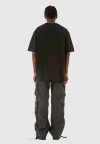Must teksas musta värvi lühikeste varrukatega oversize t-särk, millele on sobitatud laiad cargo-püksid. Mõlemad riideesemed on minimalistliku disainiga.