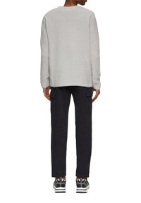 Grijze gestructureerde sweatshirt met lange mouwen, gecombineerd met donkere cargobroeken en multikleuren sneakers, gezien vanuit de achterkant.