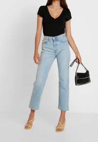 Černý bodysuit s krátkým rukávem, V-výstřihem a dřevěnými knoflíky, kombinovaný se světlými modrými džíny s vysokým pasem a malou černou kabelkou s korálky.